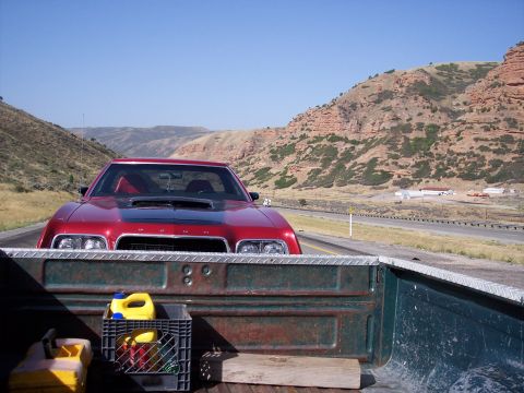 1972 Ford Ranchero - A red 1972 Ford Ranchero is seen from the perspective of a truck bed, driving on a highway through a scenic, hilly landscape.