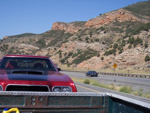 1972 Ford Ranchero - A red coupe with a hood scoop drives down a highway with mountains in the distance.