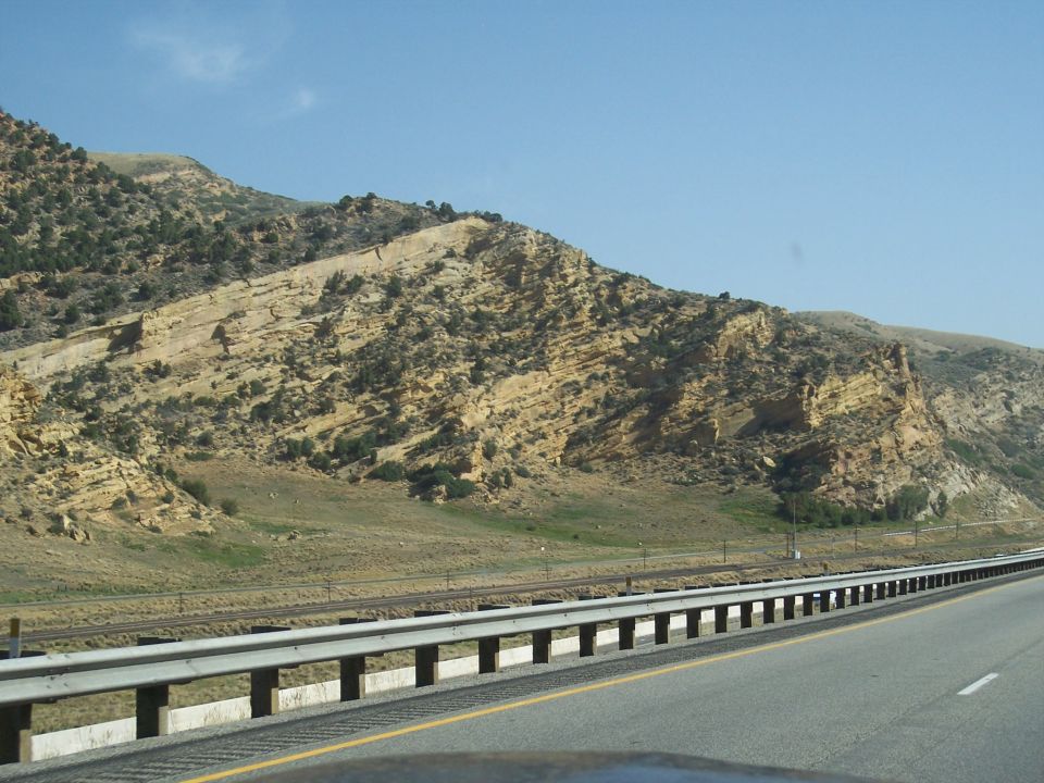 Highway passes by a rocky mountain range under a clear blue sky