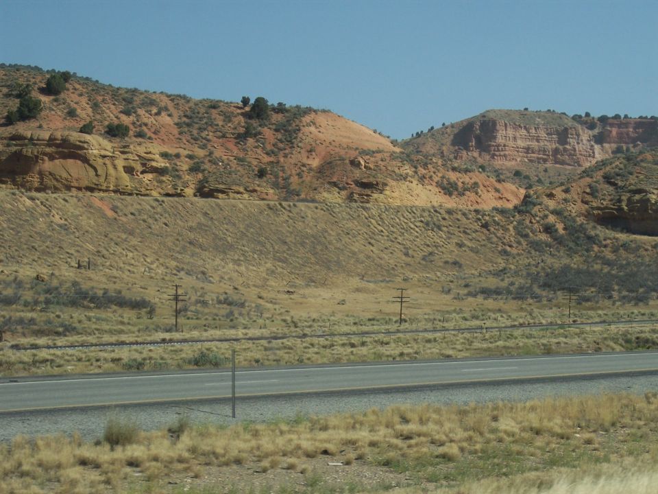 Desert landscape with red rock formations and a highway under a clear blue sky