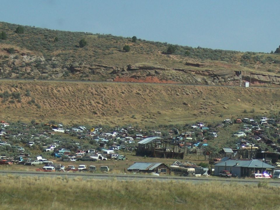 Junkyard scene with numerous old cars scattered across a hillside under a blue sky