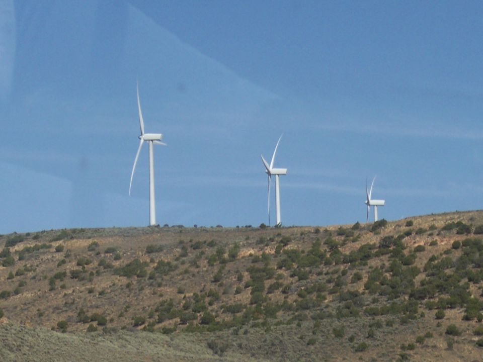 Three wind turbines stand on a barren, scrub-covered hill under a clear blue sky