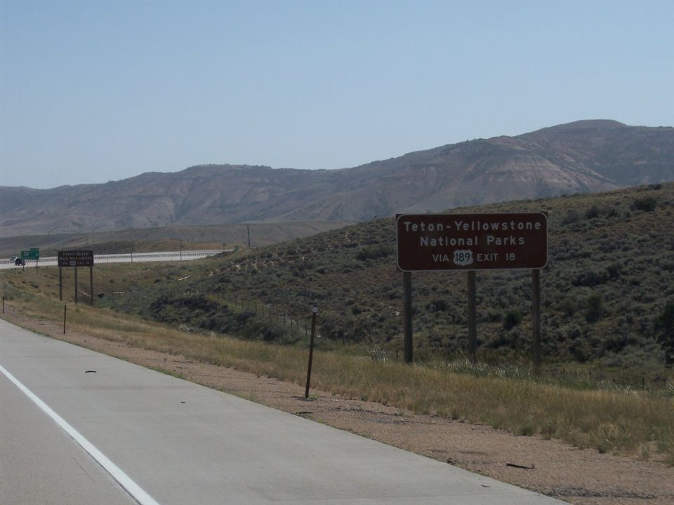 Roadside sign indicating Teton-Yellowstone National Parks via highway 189, exit 18. Mountains in background