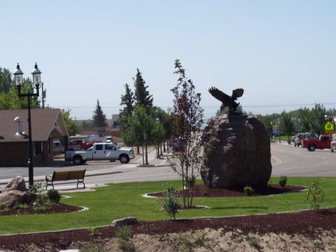 1972 Ford Ranchero - A white pickup truck is parked on the side of the road next to a building, with an eagle statue on a rock in the foreground.