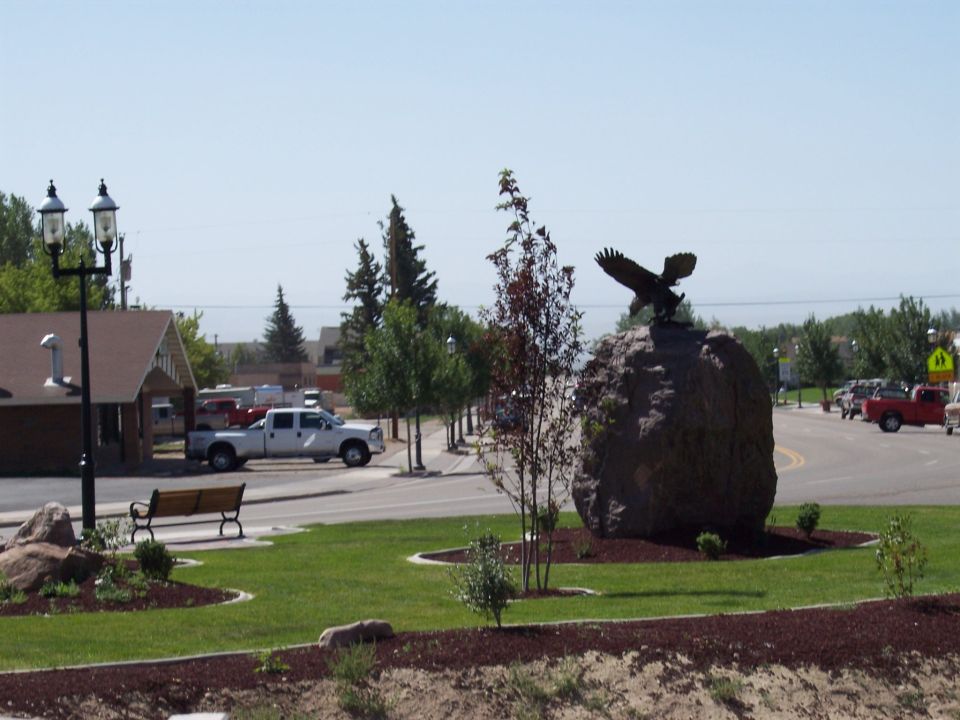 White pickup truck parked on street, eagle statue on rock in foreground