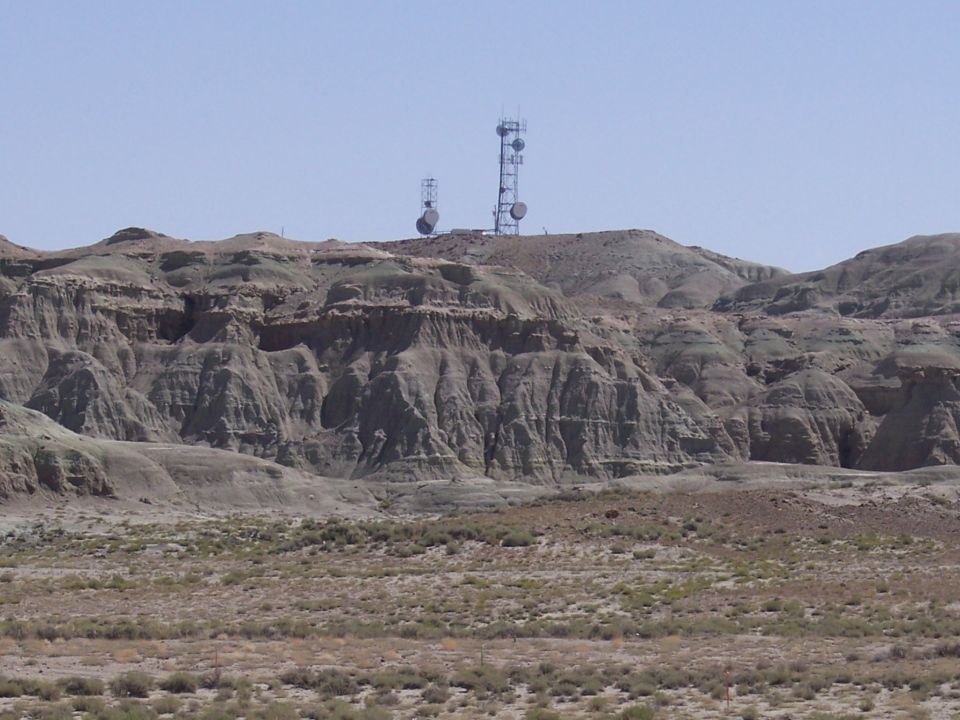 Radio towers on a barren, rocky hill under a clear blue sky