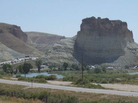 1972 Ford Ranchero - A long line of trucks travels down a highway next to a river, with a massive rock formation dominating the landscape.