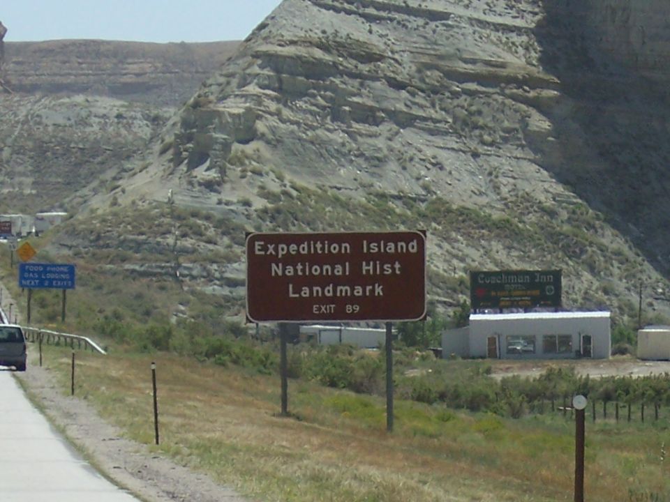 Roadside signs for Expedition Island National Historic Landmark and Coachman Inn with a mountain landscape