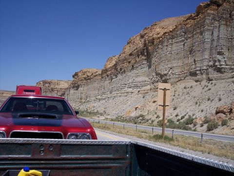 1972 Ford Ranchero - Red Dodge Charger driving on a highway with a scenic cliff face in the background.