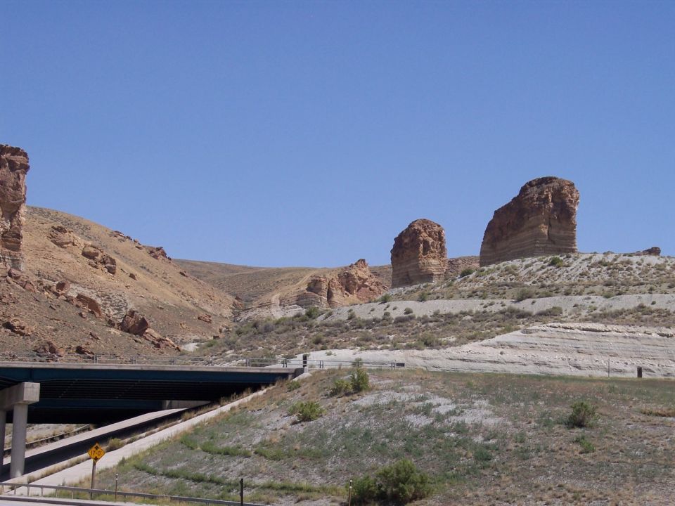 Rock formations rise above a highway overpass under a clear blue sky