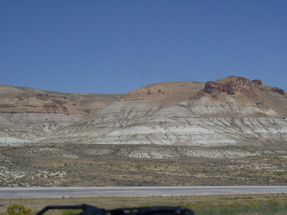 Desert landscape with layered rock formations and sparse vegetation under a clear blue sky
