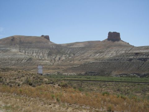 1972 Ford Ranchero - A wide view of a desert landscape two prominent mesas and a solitary billboard under a bright blue sky.