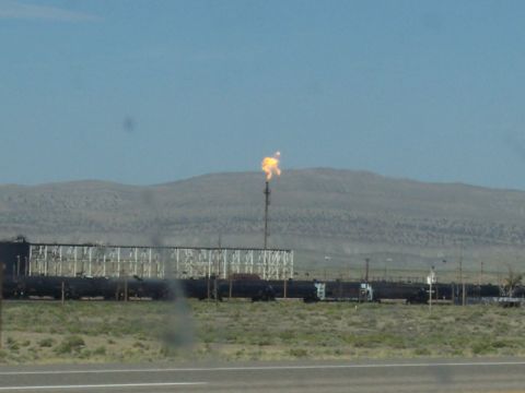 1972 Ford Ranchero - A train of tank cars is visible next to an industrial complex with a burning flare stack in the distance.