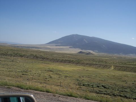1972 Ford Ranchero - A view from a vehicle's side mirror captures a wide expanse of grassland and a distant mountain under a clear blue sky.