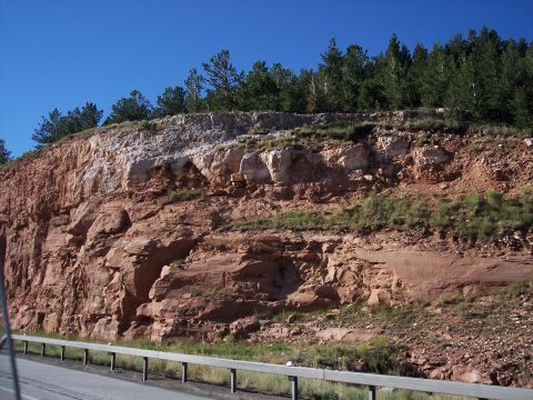1972 Ford Ranchero - A natural rock formation with layered strata, bordered by a roadside barrier and vegetation under a clear blue sky.
