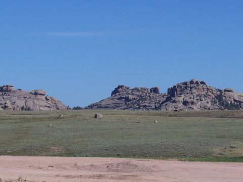 1972 Ford Ranchero - A wide landscape shot shows large rock formations against a bright blue sky, with a grassy plain below.