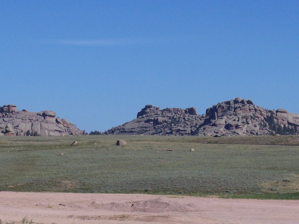 Rocky hills under a clear blue sky, with a green field in the foreground