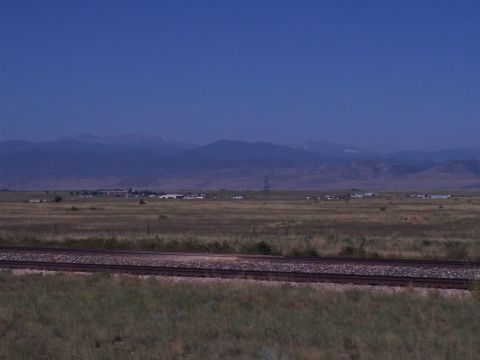 1972 Ford Ranchero - A wide landscape shot shows distant buildings and mountains under a clear blue sky, with railroad tracks in the foreground.