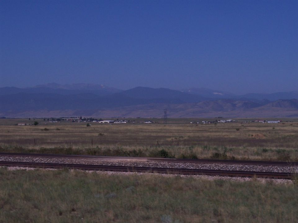 Distant buildings and mountains under a clear blue sky, with railroad tracks in the foreground