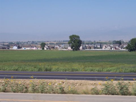 1972 Ford Ranchero - A wide view of a suburban neighborhood situated behind a large green field and a road.