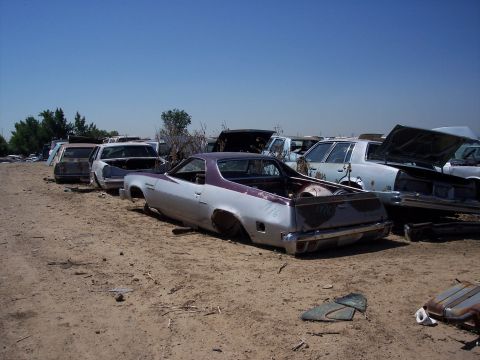 1972 Ford Ranchero - A stripped-down vehicle sits in a dusty lot filled with other discarded cars under a clear blue sky.