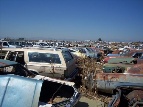 1972 Ford Ranchero - A vast junkyard filled with decaying vehicles under a bright, cloudless sky.