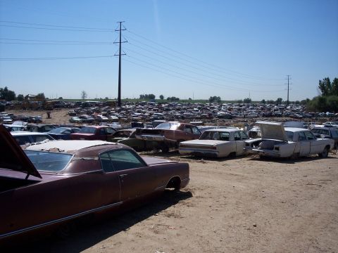 1972 Ford Ranchero - A vast junkyard filled with numerous vehicles under a bright, clear sky, suggesting a large collection of discarded automobiles.