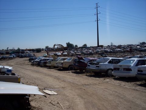 1972 Ford Ranchero - Rows of vehicles fill a junkyard lot under a bright blue sky with power lines stretching across the frame.