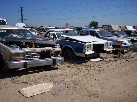 1972 Ford Ranchero - A collection of abandoned vehicles are parked in a dusty lot, awaiting their fate.