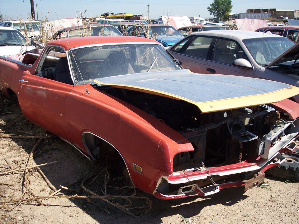 Red 1970 Ford Ranchero with hood open, missing front end parts, in a junkyard
