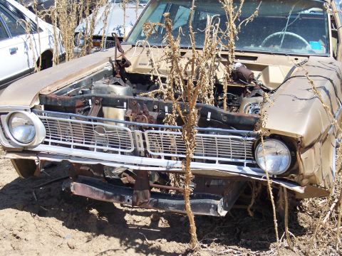 1972 Ford Ranchero - A weathered 1970 Ford Ranchero sits in a junkyard, its front end exposed and damaged.