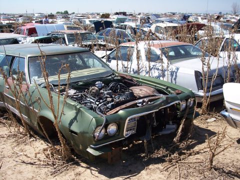 1972 Ford Ranchero - A green car sits in a junkyard, its engine exposed, with numerous other vehicles in the background.