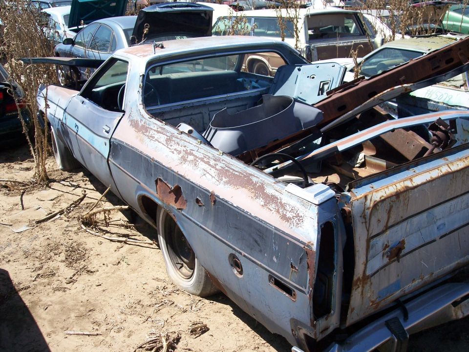 1972 Ford Ranchero in junkyard, blue with rust, rear 3/4 view, damaged
