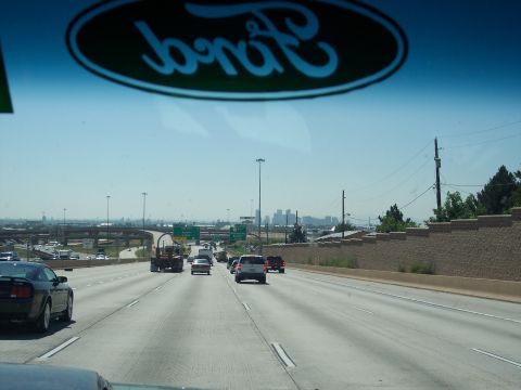 1972 Ford Ranchero - View from a vehicle on a highway, with the Ford logo visible on the windshield and a city skyline in the distance.