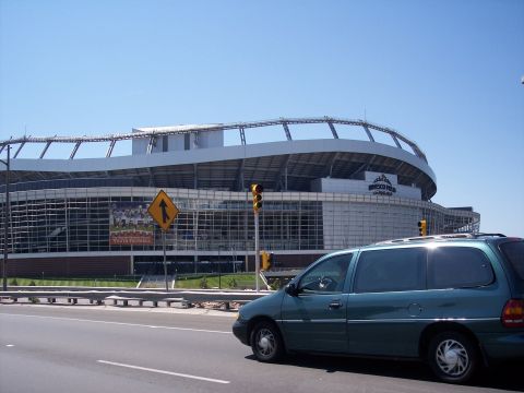 1972 Ford Ranchero - Teal minivan passes by a stadium on a sunny day.
