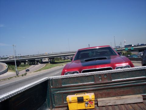 1972 Ford Ranchero - A red car with a black hood scoop is driving on the highway, viewed from the back of a pickup truck.