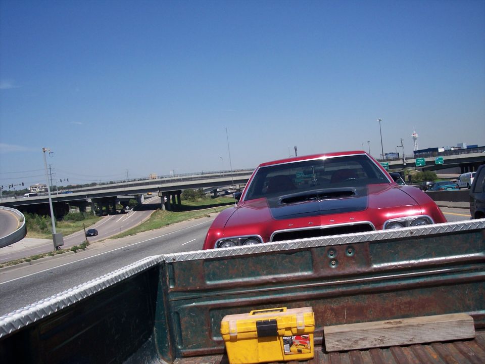 red car with black hood scoop on highway, seen from a pickup truck bed