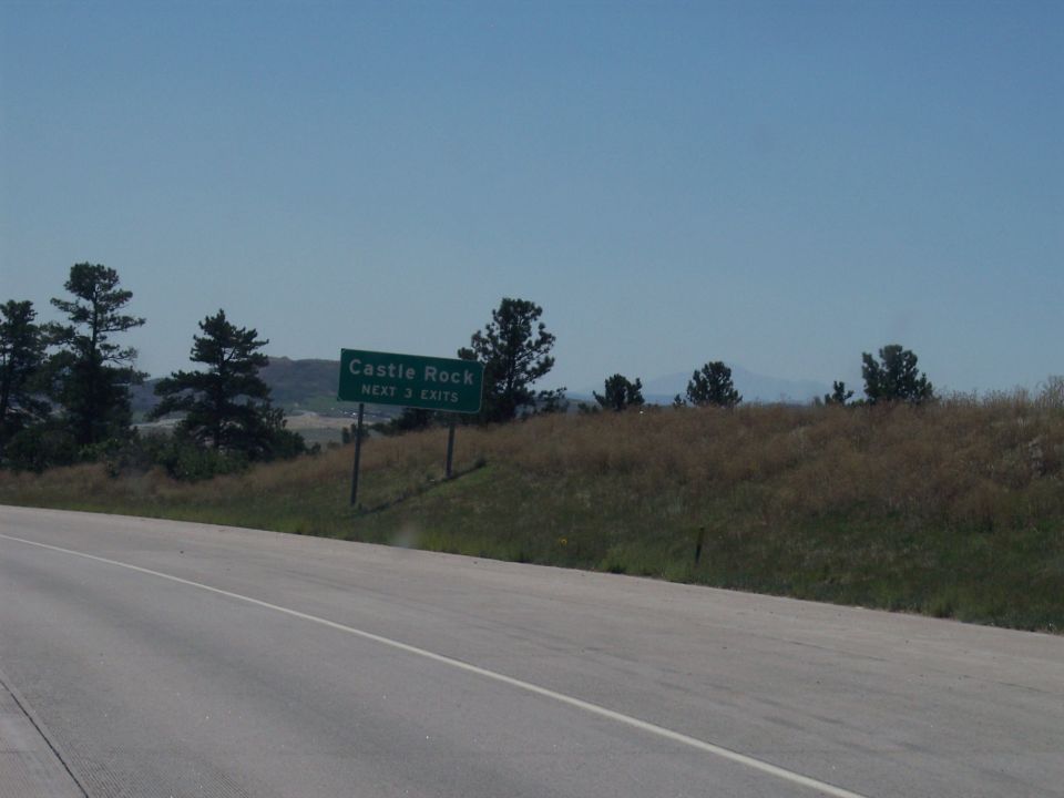 Highway sign indicating Castle Rock and next 3 exits, with trees and hills in background