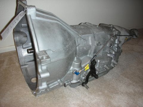 1992 Ford Crown Victoria - A silver automatic transmission is shown with its shift linkage and a white tag attached.