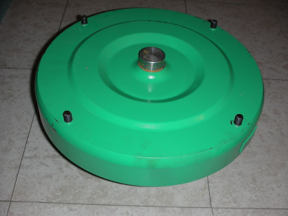Green torque converter with a silver metal shaft protruding from the center, resting on a tiled floor