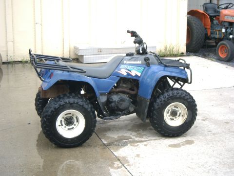 1991 Chevrolet Suburban - A blue Kawasaki Bayou ATV is parked on a wet concrete surface, with a tractor in the background.