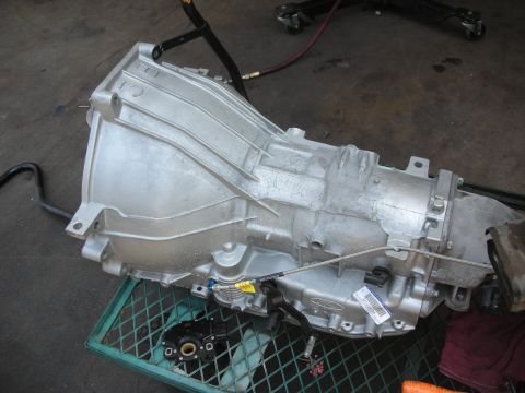 1992 Ford Crown Victoria - A silver transmission, likely from a Ford vehicle, is shown resting on a green metal grate.