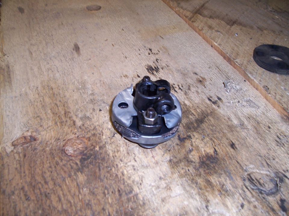Steering column U-joint with black metal yokes and a silver metal housing, resting on a wooden surface