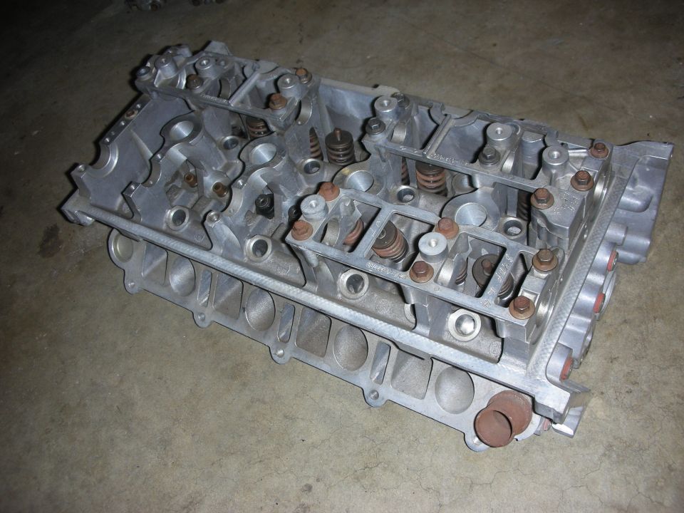 Aluminum engine cylinder head with visible valves and springs on a concrete floor