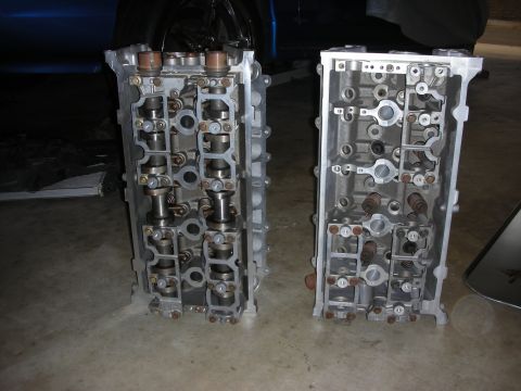 1998 Ford Crown Victoria - Two engine cylinder heads are displayed on a concrete floor, likely for sale or repair.