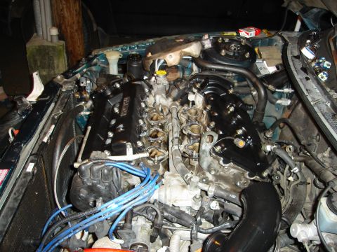 1995 Mazda MX-6 - The engine bay of a 1995 Mazda MX-6 is shown, with the valve covers painted black and blue spark plug wires visible.