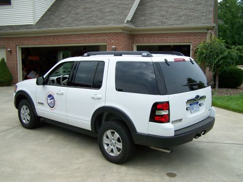 2003 Ford Crown Victoria - White Ford Explorer SUV parked in a driveway, a circular logo on the driver's side door and a license plate.