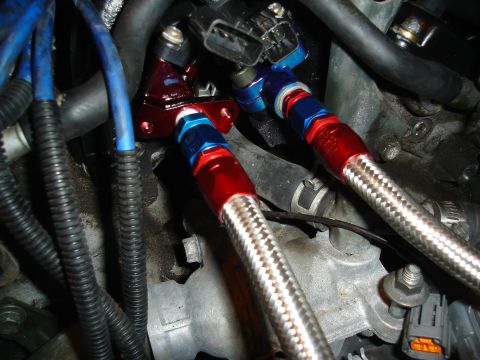 1995 Mazda MX-6 - Braided fuel lines with red and blue fittings are installed on an engine. The Supermotors logo is visible in the lower right corner.