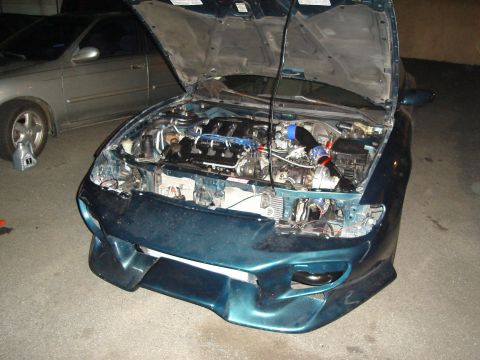 1995 Mazda MX-6 - Engine bay of a 1995 Mazda MX-6, showing modifications and a second car in the background.
