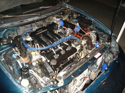 1995 Mazda MX-6 - The engine bay of a car features a V6 engine with aftermarket turbo modifications and blue hoses.